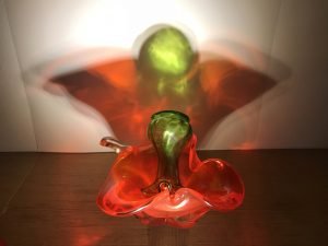 red and green glass objects refracted onto a white wall showing a red winged shape with a green head.